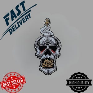 May include: Embroidered patch featuring a skull with a third eye, an ankh, and the text "MUD BASE." The skull has red accents around the eyes and is surrounded by a white smoke-like design. The patch is labeled "BEST SELLER" and "HIGH QUALITY."