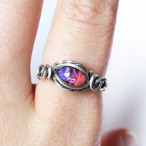 May include: A silver wire wrapped ring with a pink and purple oval shaped gemstone.