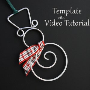 Könnte beinhalten: Silberner Draht-Schneemann-Anhänger mit einem rot-weiß karierten Schal. Der Anhänger hängt an einem grünen Band. Der Text "Template with Video Tutorial" ist im Hintergrund sichtbar.