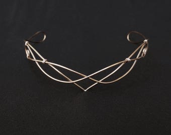 Puede incluir: Una corona de alambre dorado con un diseño delicado e entrelazado. La corona está hecha de alambre fino y tiene un estilo simple y elegante.