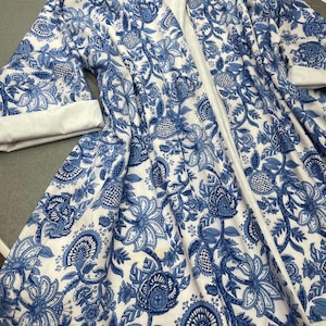 May include: A white and blue floral patterned robe. The robe features a detailed design of blue flowers and leaves against a white background. The robe has long sleeves with white cuffs and a white interior lining.