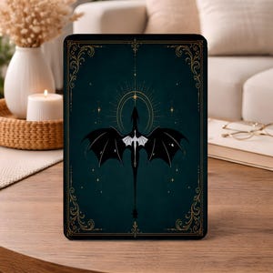May include: A rectangular tablet case featuring a dark teal background with a central black dragon illustration. The dragon has outstretched wings and is positioned beneath a golden starburst design. The border is decorated with gold filigree.