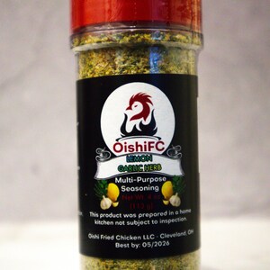 May include: A clear plastic bottle with a red cap, filled with lemon garlic herb seasoning. The label features a logo with a red bird and the text "OishiFC Lemon Garlic Herb Multi-Purpose Seasoning". The net weight is 4 oz (113 g).