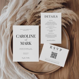 May include: A wedding invitation suite comprising three white cards with black text. The main card announces "Caroline and Mark" with event details. A second card lists reception details, and the third is an RSVP card with a QR code.