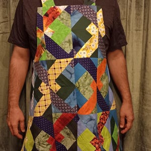 May include: A patchwork apron in a vibrant array of colours and geometric designs. The apron incorporates blues, greens, oranges, and yellows, with a quilted appearance. The straps are also made from patchwork fabric.