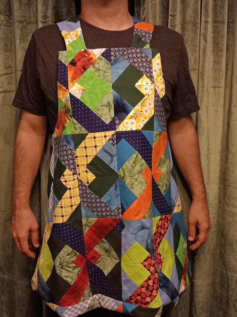 May include: A patchwork apron in a vibrant array of colours and geometric designs. The apron incorporates blues, greens, oranges, and yellows, with a quilted appearance. The straps are also made from patchwork fabric.