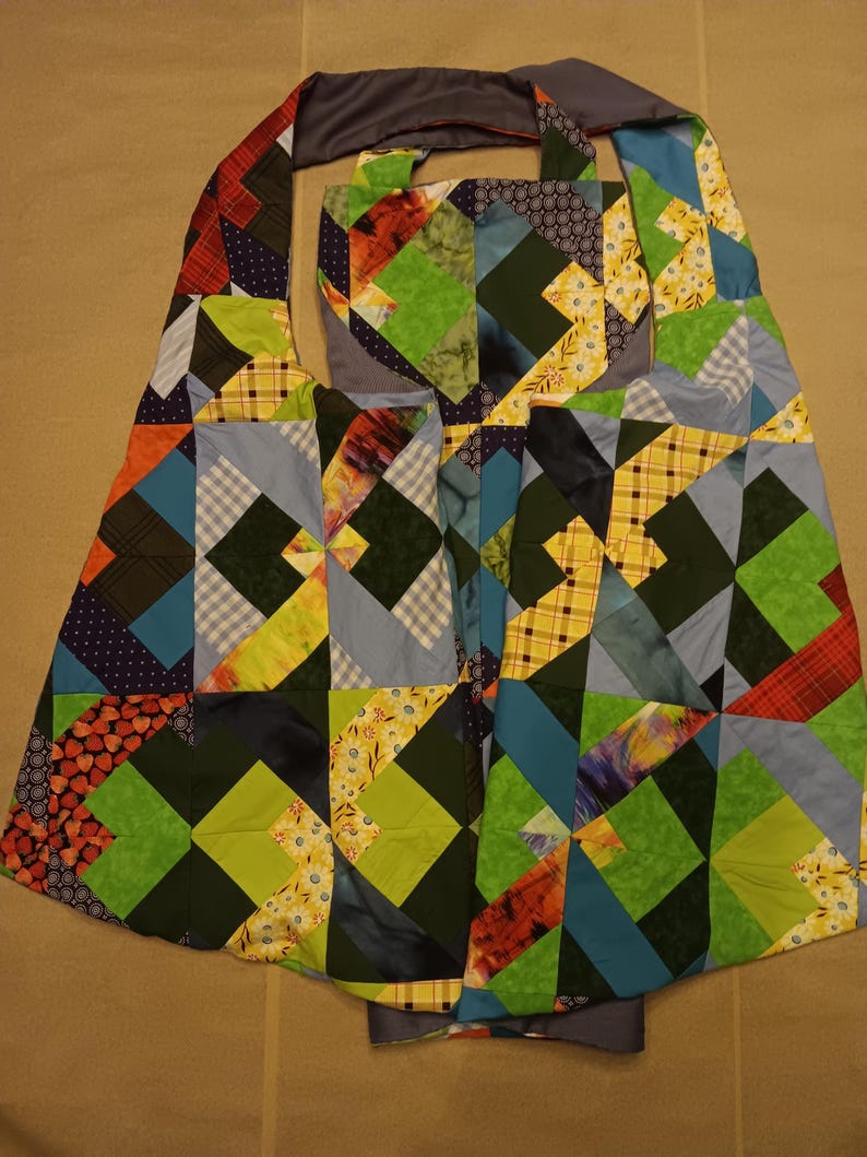 May include: A patchwork tote bag with a geometric design. The bag features a variety of fabrics in shades of green, blue, orange, and yellow. The bag has a grey strap and a grey lining.