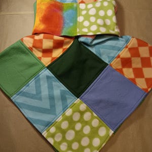 May include: A patchwork fleece hooded poncho in a variety of colors and patterns. The hood features orange, blue, and green tie-dye, orange and white checkered, and green with white polka dots. The poncho's body has green, blue, dark green, and orange checkered squares.