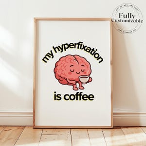 Peut inclure: Une affiche encadrée avec un cerveau de dessin animé tenant une tasse de café. Le texte dit "my hyperfixation is coffee". Le cerveau est rose, et le texte est noir et jaune. L'affiche est dans un cadre en bois.