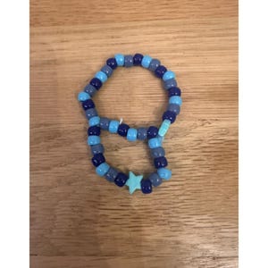 Puede incluir: Un bozal de cuentas azules con un dije en forma de estrella. El bozal está hecho de varios tonos de cuentas azules y tiene el texto "SMALL MUZZLE" en azul en la parte superior.