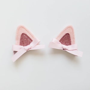 May include: A pair of pink felt cat ears with glitter accents and matching pink satin bows.