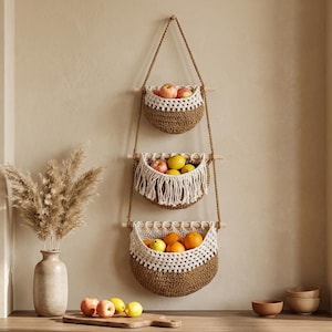 May include: Three-tiered hanging fruit baskets made of brown woven material with white crochet trim. Each basket is filled with fresh fruit, including apples, lemons, and oranges. The baskets hang from a natural rope and wooden dowels, creating a rustic, farmhouse aesthetic.