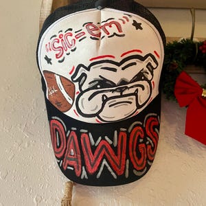 May include: Black and white trucker hat with a bulldog graphic and the words "Sic 'em Dawgs" in red. The hat features a mesh back and a curved brim, perfect for sports fans.