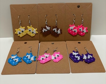 May include: Six pairs of handmade beaded earrings in various colors, including yellow, brown, pink, blue, and purple. Each pair features a unique design and is displayed on a brown card. The earrings have silver-colored hooks.