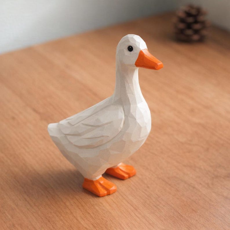 May include: A white goose figurine with a faceted, geometric surface texture. The bird features a bright orange beak and matching orange webbed feet. It has a small black eye and is standing in a profile position, showcasing its angular, carved design.