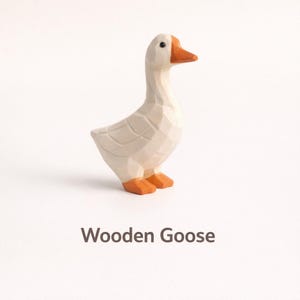 May include: A carved wooden goose figurine with a faceted surface texture. The goose is painted in an off-white color with a bright orange beak and orange feet. A small black dot serves as the eye. The text "Wooden Goose" appears below the figure.