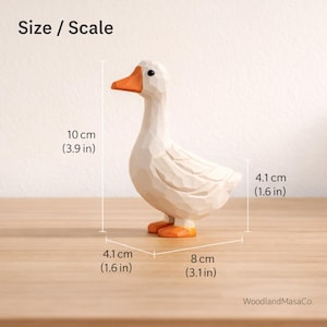 May include: A carved wooden goose figurine with a white body and orange beak and feet. The figure features faceted surfaces and measures 3.9 inches in height, 1.6 inches in width, and 3.1 inches in length. Text reads Size / Scale and WoodlandMasaCo.