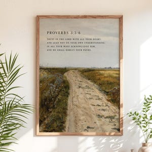 May include: A framed print featuring a dirt road winding through a field, with text from Proverbs 3:5-6. The artwork has a vintage aesthetic, with a neutral color palette and a wooden frame. The print is displayed above a wooden cabinet.