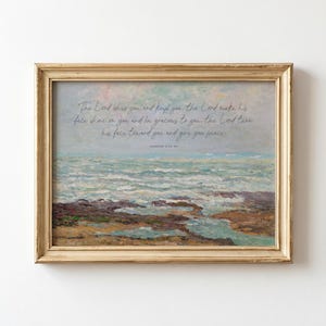May include: A landscape painting in a gold frame depicting a rocky shoreline and ocean waves under a soft sky. The text reads: The Lord bless you and keep you; the Lord make his face shine on you and be gracious to you; the Lord turn his face toward you and give you peace. Numbers 6:24-26.