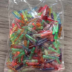 May include: A clear plastic bag filled with a multitude of small, colorful light bulbs. The bulbs are various shades of red, green, blue, yellow, and purple. The bag is sitting on a wooden surface.