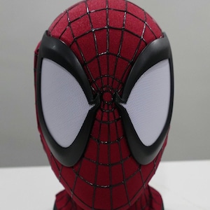 Op de afbeelding: Een rood en zwart Spider-Man masker met witte mesh oogbedekkingen. Het masker heeft een webpatroon en zwarte randen rond de ogen. Het masker is een kostuumaccessoire.