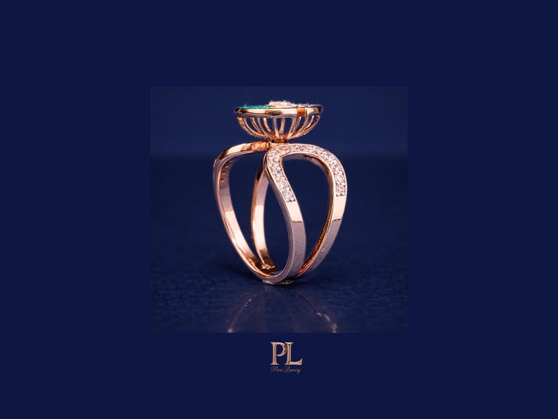May include: Rose gold ring with a unique design. The ring features a central emerald-colored stone and is accented with small diamonds. The band has a double-loop design, with diamonds set along the curves. The ring is set against a dark blue background.