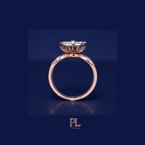 May include: A rose gold ring with a floral design, featuring a cluster of small, light blue gemstones at the center. The band is adorned with small, clear stones. The ring is set against a dark blue background.