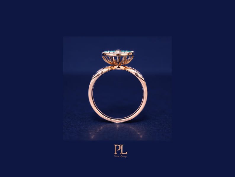 May include: A rose gold ring with a floral design, featuring a cluster of small, light blue gemstones at the center. The band is adorned with small, clear stones. The ring is set against a dark blue background.