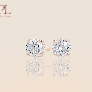 May include: A pair of rose gold stud earrings with round, brilliant-cut diamonds. The earrings are set in a four-prong setting, reflecting light. The earrings are displayed on a reflective surface. The logo "PL Pure Luxury" is in the upper left corner.