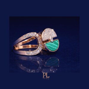 May include: Rose gold ring with a unique design. The ring features a section of sparkling white diamonds and a section of green malachite. The ring's design includes a split band and a geometric shape.