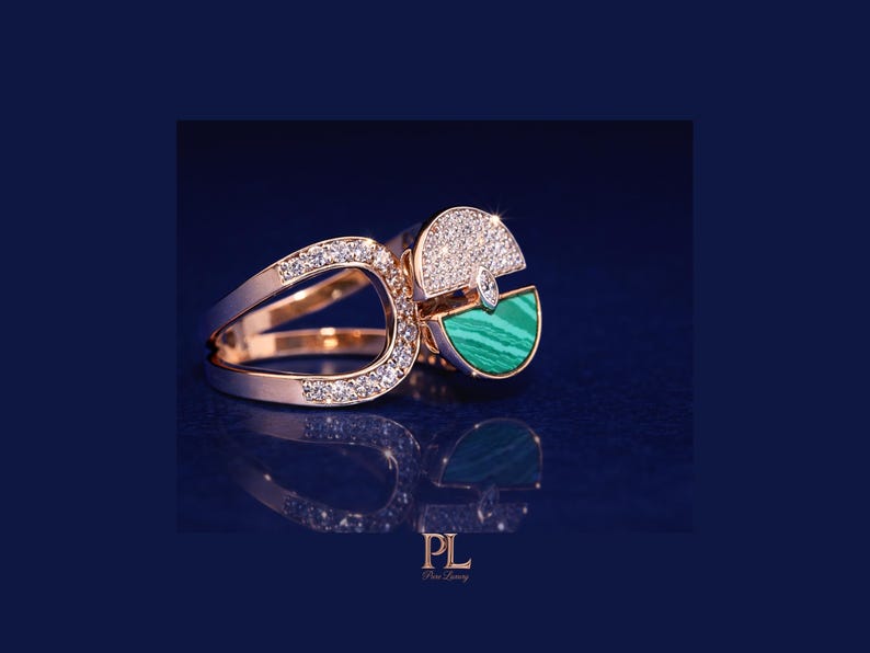May include: Rose gold ring with a unique design. The ring features a section of sparkling white diamonds and a section of green malachite. The ring's design includes a split band and a geometric shape.