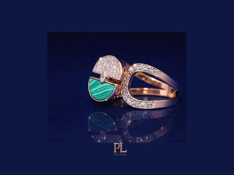 May include: A gold ring with a unique design, featuring a half-circle of sparkling diamonds and a section of green malachite. The ring has a split band and is set against a dark blue background.