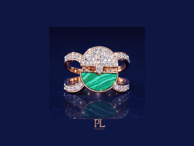 May include: Rose gold ring featuring a half-circle of sparkling diamonds and a half-circle of green malachite. The ring has a unique design with diamond accents on the band. The ring is displayed on a dark blue background.