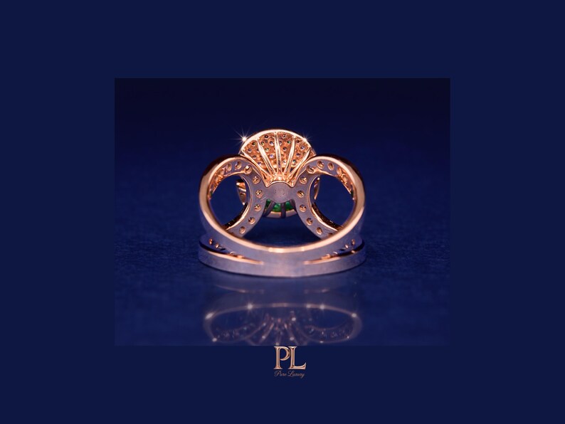 May include: A rose gold ring with a large, round green gemstone at the center, surrounded by smaller clear stones. The ring has a double band design with intricate detailing and is set against a dark blue background.
