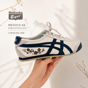 以下が含まれることがあります： Onitsuka Tiger MEXICO 66 スニーカー。バーチとピーコートのカラーリングで、ローカットシルエット、レースアップクロージャー、特徴的なサイドストライプ、サイドパネルに花の刺繍が施されています。テキストにはOnitsuka Tiger MEXICO 66と記載されています。