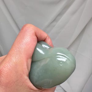 Puede incluir: Una talla de piedra verde p&aacute;lido de una ballena. La ballena se sostiene en una mano y la piedra tiene un acabado brillante. La talla tiene un dise&ntilde;o simple y redondeado con detalles sutiles.