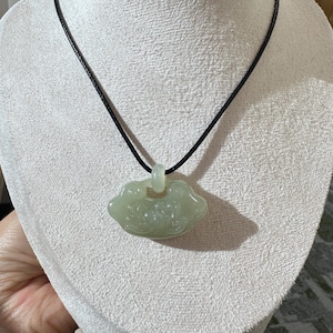 May include: A light green jade pendant necklace. The pendant is a cloud shape with carved details, suspended from a black cord. The necklace is displayed on a white mannequin.