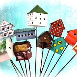 May include: A collection of colorful, miniature birdhouses on metal stakes. The birdhouses feature various designs, including polka dots, stripes, and painted details. The color palette includes red, green, blue, and brown, creating a whimsical and decorative display.