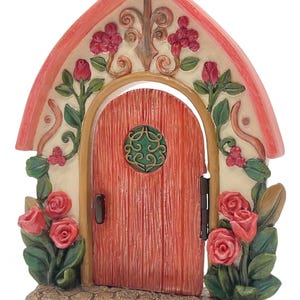 May include: A miniature fairy door with a red door and a pink arched roof. The door is adorned with red roses, green leaves, and a decorative green circle. The base is a stone-like texture.