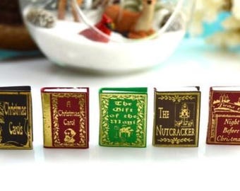 May include: Miniature Christmas-themed books with gold accents. Titles include "Christmas Carols", "A Christmas Carol", "The Gift of the Magi", "The Nutcracker", and "Twas the Night Before Christmas". The books are arranged in a row.