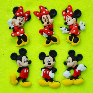 May include: Six colorful cartoon character figurines. Three are Minnie Mouse, wearing red dresses with white polka dots and red bows. The other three are Mickey Mouse, wearing red shorts and yellow shoes. All are on a bright green background.