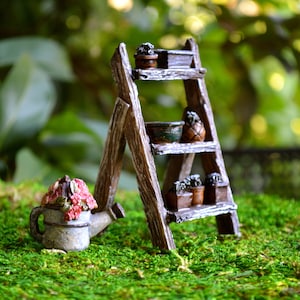 May include: Miniature wooden ladder shelf with small potted plants and a watering can with pink flowers. The ladder has three shelves with various pots and a rustic, weathered appearance. The watering can is gray.