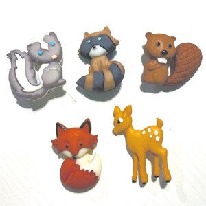 May include: A collection of five woodland animal figurines: a skunk, raccoon, beaver, fox, and deer. The skunk is gray and white, the raccoon has a striped tail, the beaver has a large tail, the fox is red and white, and the deer is yellow with white spots.