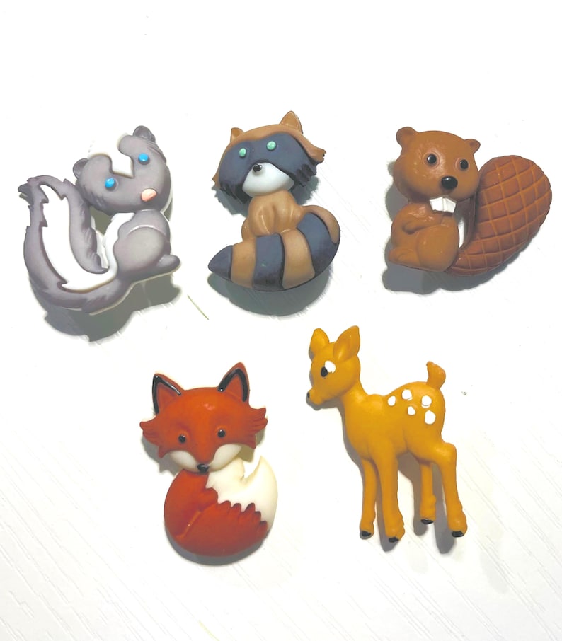 May include: A collection of five woodland animal figurines: a skunk, raccoon, beaver, fox, and deer. The skunk is gray and white, the raccoon has a striped tail, the beaver has a large tail, the fox is red and white, and the deer is yellow with white spots.
