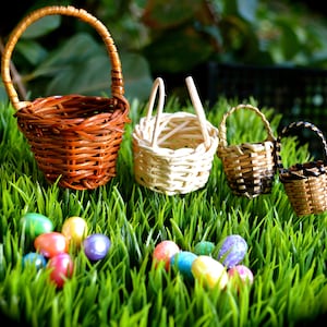 May include: Four miniature woven baskets in varying shades of brown and beige sit on a bed of green grass, alongside colorful Easter eggs. The baskets have handles and are intricately woven, showcasing a rustic charm.