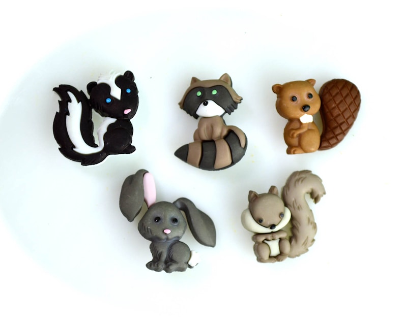 May include: A collection of five woodland animal figurines: a skunk, raccoon, beaver, bunny, and squirrel. The skunk is black and white, the raccoon has a striped tail, the beaver has a large tail, the bunny has pink ears, and the squirrel has a bushy tail.