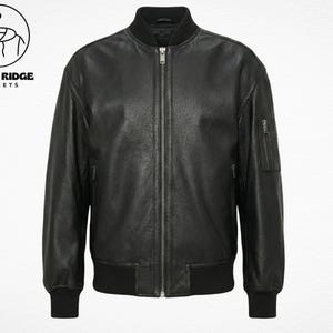 Peut inclure: Veste de bombardier en cuir noir avec fermeture éclair, poignets et ourlet côtelés. La veste a deux poches latérales et une petite poche sur la manche gauche. Le logo Retro Ridge Jackets est dans le coin supérieur gauche.