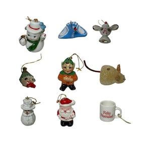 May include: A collection of vintage Christmas ornaments. The ornaments include a snowman, a blue bird, a mouse, an elf, a Santa Claus, and a mug with the text "Feliz Navidad". Each ornament has a gold string for hanging.