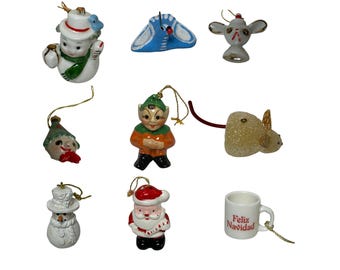 Puede incluir: Una colección de adornos navideños vintage. Los adornos incluyen un muñeco de nieve, un pájaro azul, un ratón, un elfo, un Papá Noel y una taza con el texto "Feliz Navidad". Cada adorno tiene una cuerda dorada para colgar.