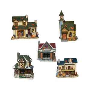 May include: A collection of five miniature ceramic buildings, including a church, a toy shop, and houses. The buildings feature detailed designs with autumn-themed decorations like pumpkins and fall foliage. The color palette includes shades of green, yellow, and brown.